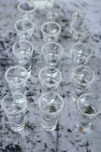 Neatly arranged shot glasses with a salt rim, filled with clear alcohol, prepared for a party or celebration on a stylish grey background