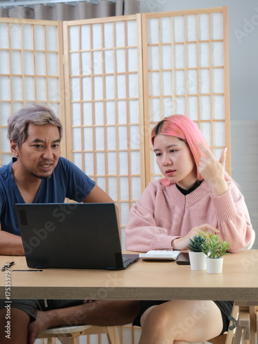 A woman with pink hair is typing on a laptop