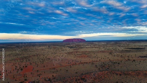 Foto Majestic Uluru, the iconic red sandstone monolith, rises against a dramatic sky at sunset in the Australian outback