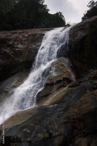 Cascading waterfall plummeting over rocky cliff in lush, verdant forest.