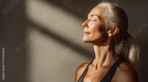 A senior  woman with long gray hair is meditating in a serene environment. Soft light illuminates her face, highlighting her calm expression.