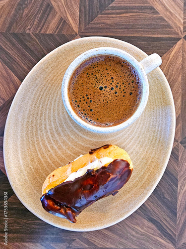 Cup of coffee and eclair on wooden table. Top view