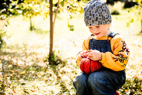 Joyful child outdoors surrounded by pumpkins and leaves