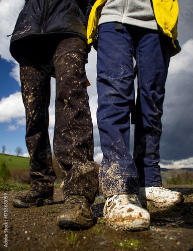 Two people standing outdoors with muddy shoes and dirty pants after hiking on a wet trail. Adventure, travel, and nature concept showing authentic outdoor experience and active lifestyle.