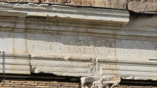 Rome, Italy - 13 January 2025. Partial Latin text carved into a cracked marble frieze at the Portico of Harmonious Gods, with erosion and chipping on the lower edge.