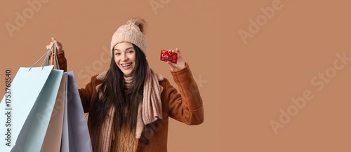 Young woman in warm clothes, with gift card and shopping bags on brown backgr...