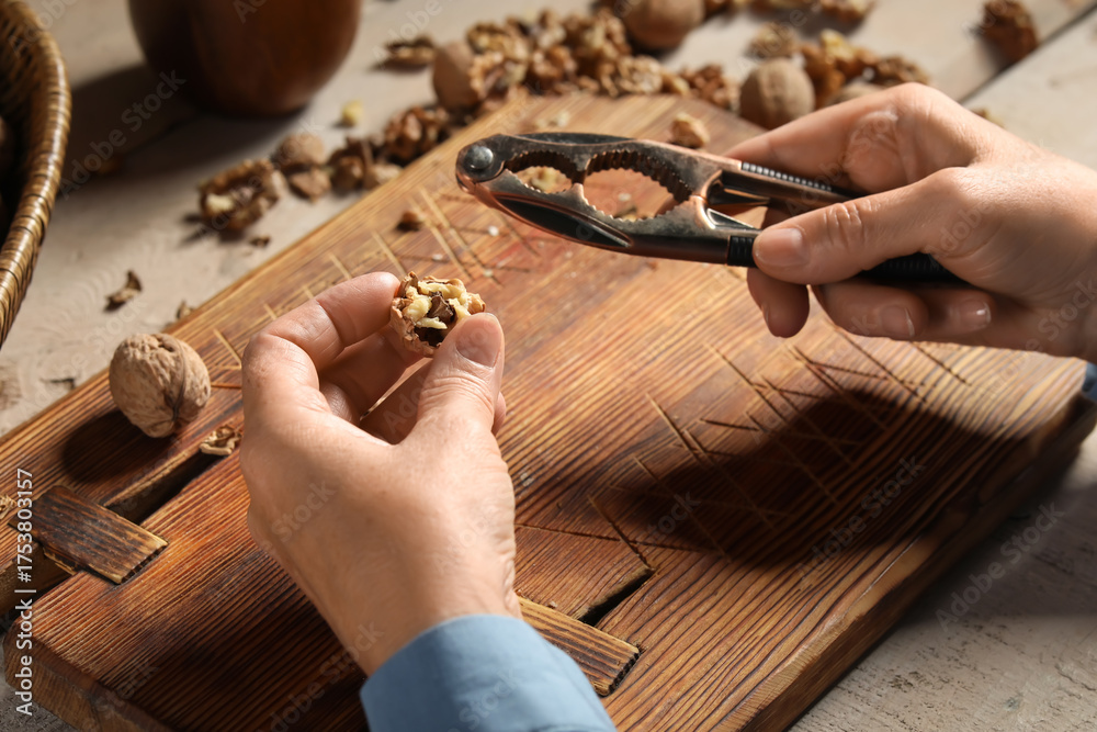 Fototapeta premium Elderly woman cracking walnuts with nutcracker on wooden table