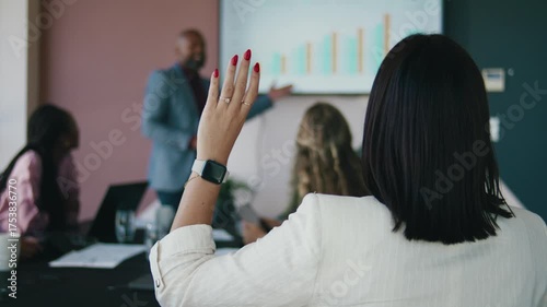 Back view of businesswoman with hand raised asking query during presentation in meeting room