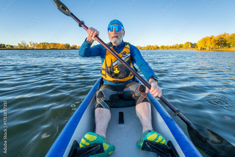 Obraz premium Senior male paddler in his 70s is paddling an inflatable touring kayak on a calm, serene lake in Colorado in fall scenery.