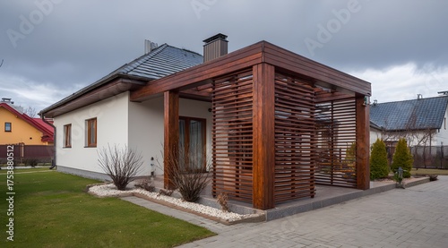 Modern house with wooden pergola and manicured lawn under cloudy sky.