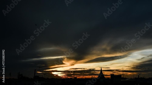 Real-time transition from dark, moody skies to a bright sunrise, captured over the silhouette of a Thai pagoda or stupa in a bustling city. This authentic, non-AI generated video