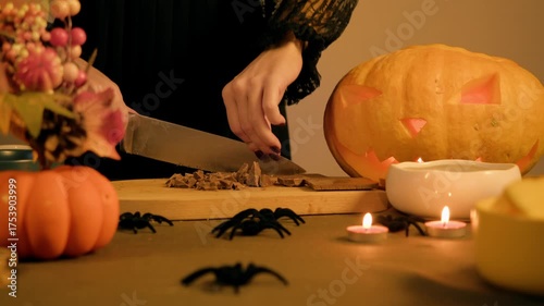Sharp knife crushes chocolate bar into chunks on a board, table is decorated for a holiday with Halloween spiders