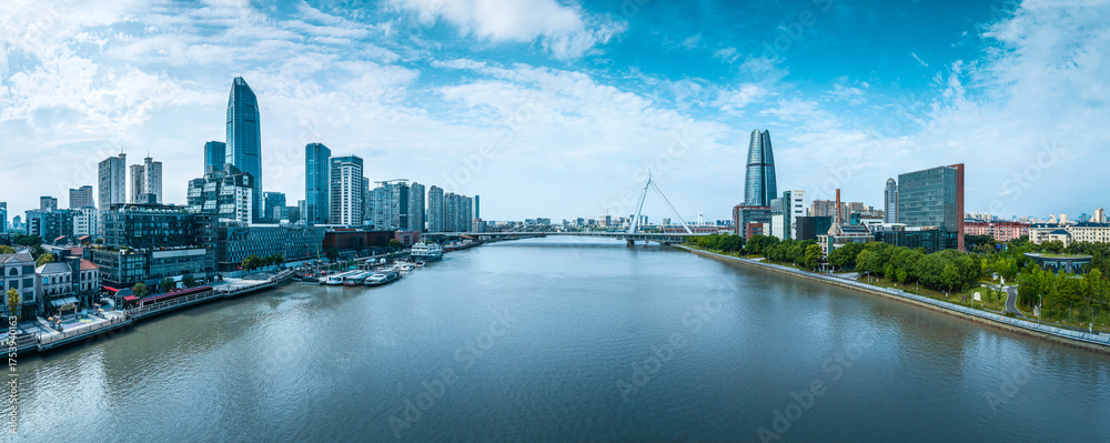 Fototapeta premium Panoramic cityscape of the modern financial district with a cable-stayed bridge crossing the wide river under a blue sky in Ningbo.