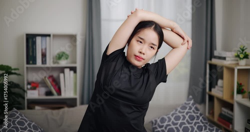 Handheld front view shot, Relaxed Asian woman is exercising by stretching in the living room at home. Healthy Lifestyle Concepts. Women Lifestyle
