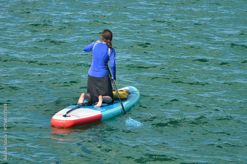 Obraz premium Young woman riding on an inflatable paddle board.