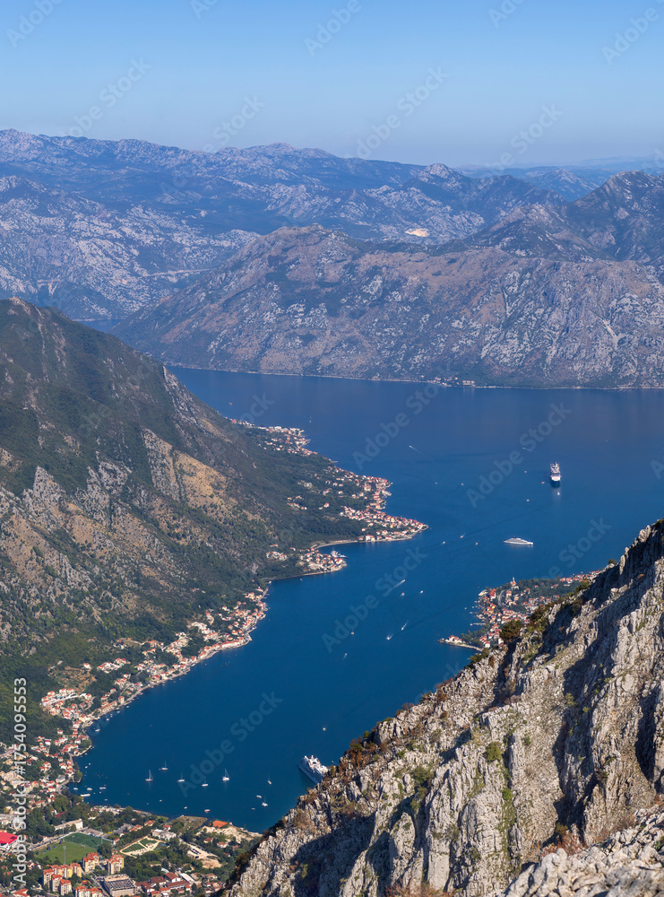 Obraz premium Panoramic view of the Bay of Kotor and Tivat, Montenegro, from the Lovcen National Park showing blue sea, rugged mountains, and scenic coastline under clear sky.