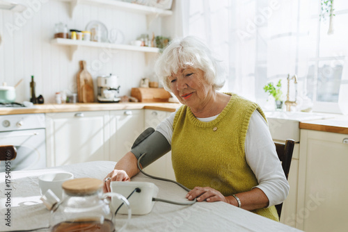 Bild auf Leinwand Indoor image of caucasian senior lady with gray hair doing morning routine measurement of her blood pressure with manual aneroid or monitor to stay healthy sitting at kitchen table