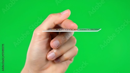 Human hand displaying the remarkable thinness of a modern, card-like object on a bright green studio background