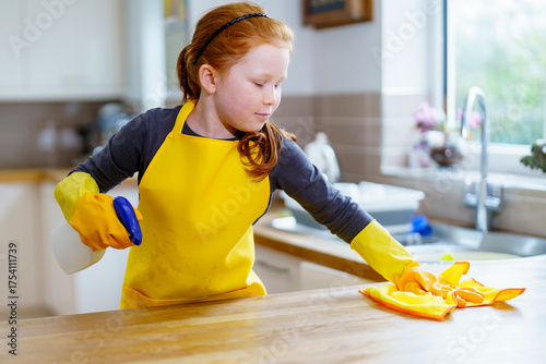 Photos Child cleaning kitchen counter with spray bottle and cloth in bright home settin