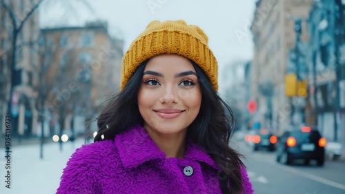 A woman smiles serenely in a urban setting, enjoying a crisp winter day. She is warmly dressed and is the focal point in the snowy city