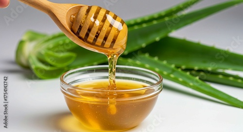 honey dripping from a wooden spoon, Wooden spoon pouring agave nectar into a glass bowl. Healthy sweet liquid dripping from spoon. Aloe vera leaves alongside syrup. Concept of natural sweetener and he