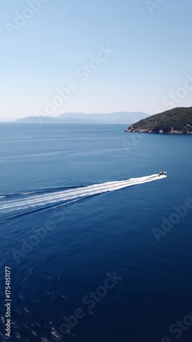 A speedy boat cuts through deep blue waters near a green island, leaving a white wake under a clear sky