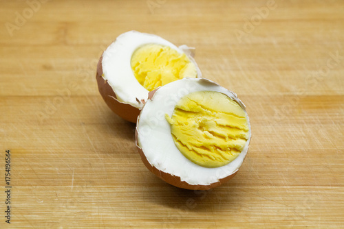 a boiled egg in its shell, cut in half, showing the texture of the white and yolk against the background of a wooden board