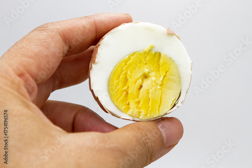 the hand holds half a boiled egg, showing the texture of the white and yolk