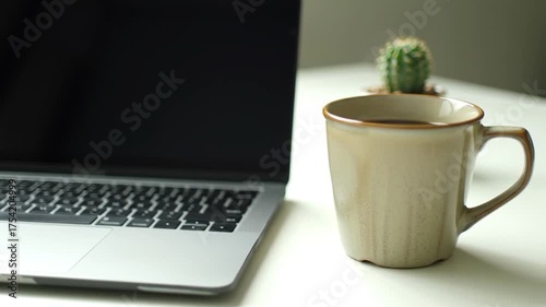 Modern workspace with a laptop, ceramic coffee mug, and a tiny potted cactus on a bright desk