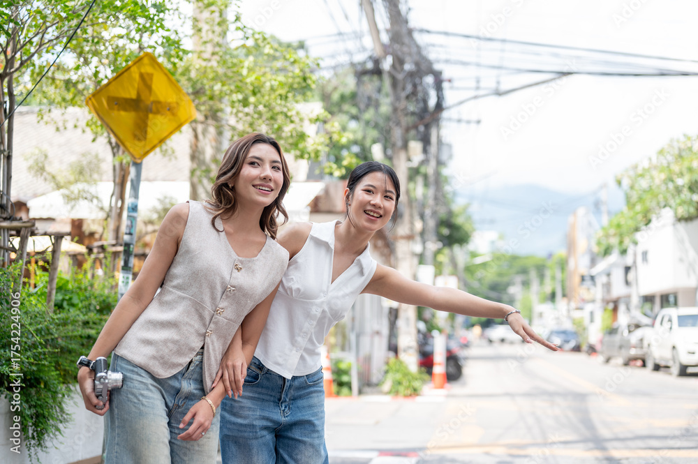 Naklejka premium Pretty asian woman holding camera and friend calling taxi while standing on sidewalk by street road.