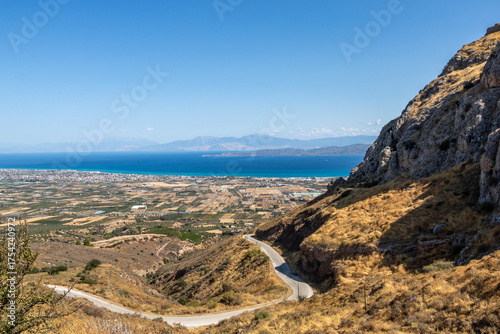 Scenic road leading to the ancient Acrocorinth hill overlooking the Corinthian plain and the blue sea in the distance
