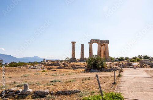 Ruins of the Temple of Apollo in Ancient Corinth, Greece. The surviving Doric columns stand against a clear blue sky, a symbol of classical Greek architecture.