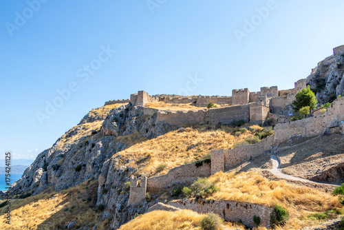 View of the medieval fortress on the slopes of Acrocorinth hill, surrounded by dry summer grass and blue sky. Historic landmark of the Peloponnese.