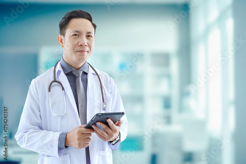 Portrait of asian senior doctor standing while using tablet in Examination Room COPY SPCAE.