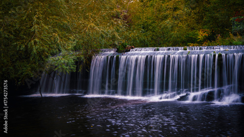 Water of Leith waterfall in Dean Village, Edinburgh, Scotland, a tranquil, silky flow beneath weeping willow branches in a quiet urban hollow.