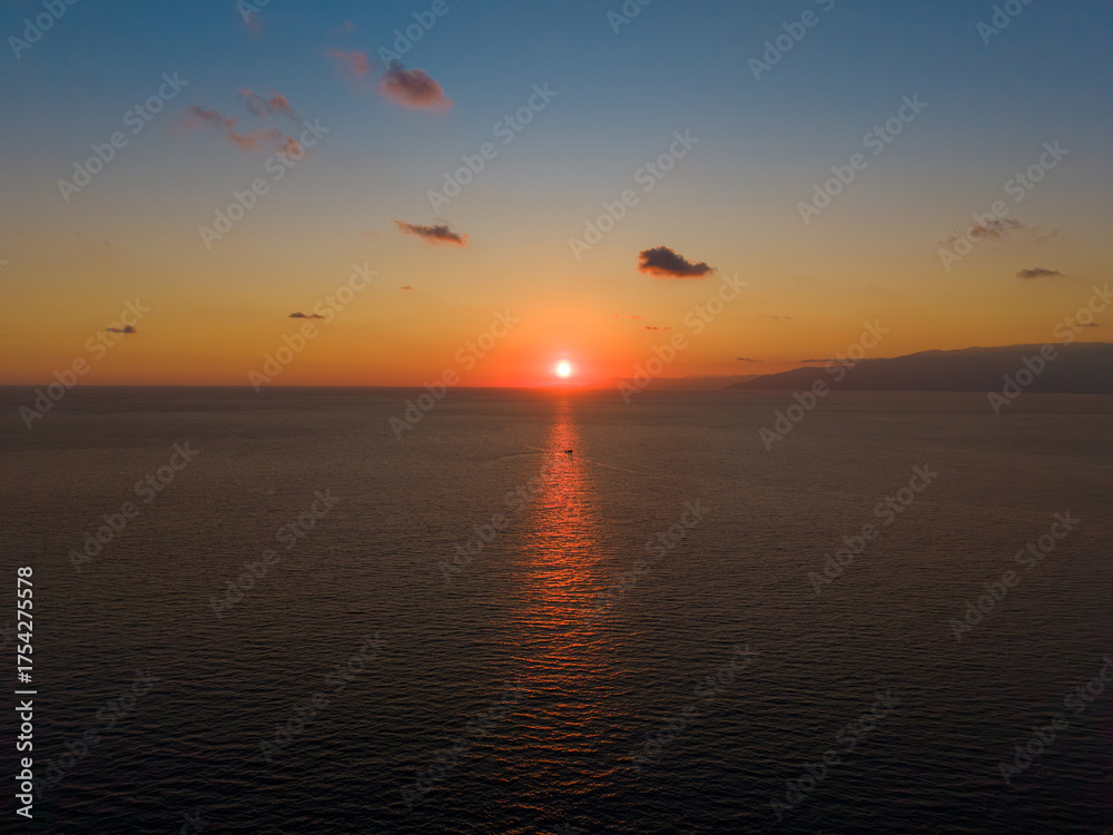 Naklejka premium Golden sunset reflecting on sea with a small boat in reflection