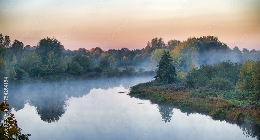 Fototapeta premium Morning mist over a calm river with trees and reflections at sunrise