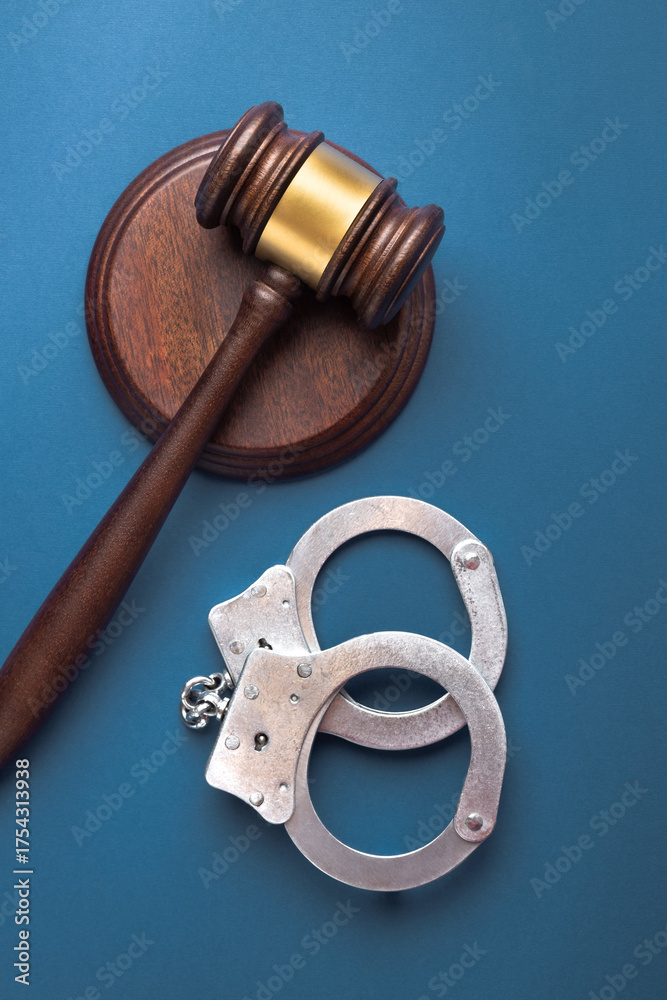 Obraz premium Judge gavel and handcuffs on a blue surface. Symbolizes courtroom authority and enforcement. Top view, flat lay.