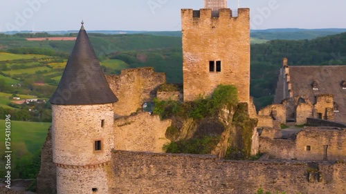 bourscheid castle château de green cover hills walls towers flags upper exterior old ruins historical site to left around right up close drone panning 