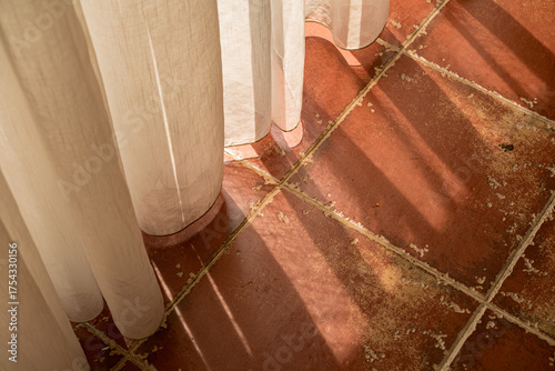 Sunlight casting shadows through a sheer curtain onto terracotta floor tiles and a glass door