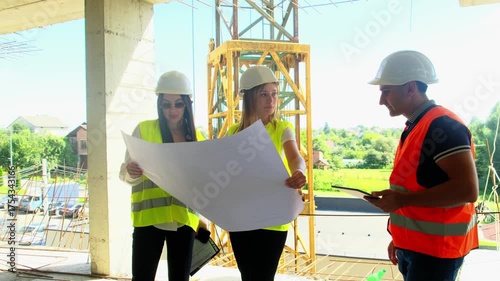 Construction team with helmets review architectural plans at building site. Engineers and taskmaster checks project progress with blueprint indoors