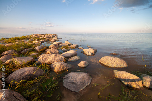 A tranquil scene of a rock beach with wet stones during sunrise, offering a path to the water's edge.