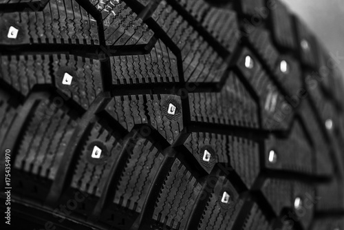 A brand new black studded car tire with metal studs embedded within the tread