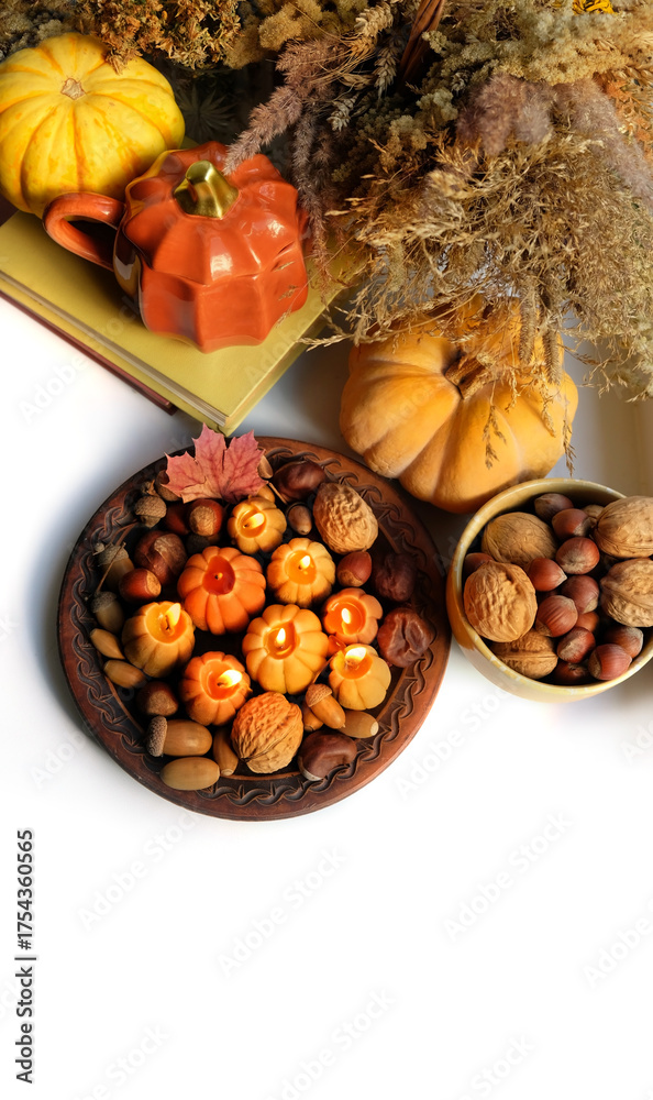 Fototapeta premium Autumn background. Pumpkin shape cup, nuts, pumpkin, decorative candles, books on white table. cozy composition for fall season, Mabon, Halloween, Thanksgiving holidays. top view. copy space