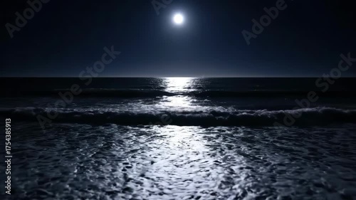 Bright moon reflecting on the dark ocean at night. A shimmering moonlight path on the water as waves roll onto the beach. Natural nighttime seascape