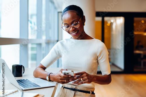 Professional woman using a smartphone at desk with a laptop