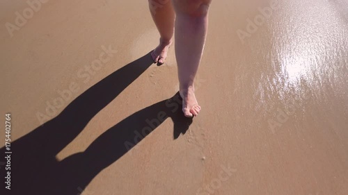 Women's feet walking barefoot on the beach, water splashing on their feet