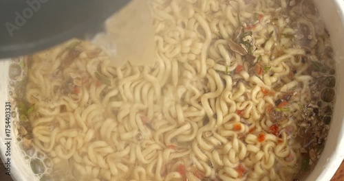 Instant noodles with spices are poured with boiling water, top view.