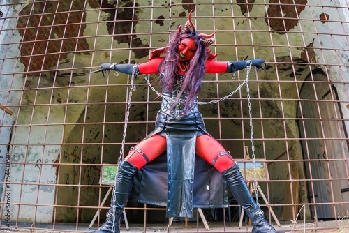 Demonic cosplay woman with horns and chains behind metal bars