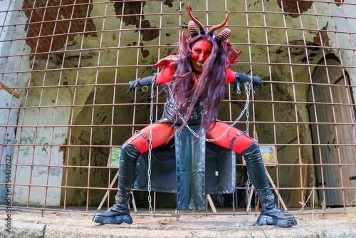Demonic cosplay woman with horns and chains behind metal bars